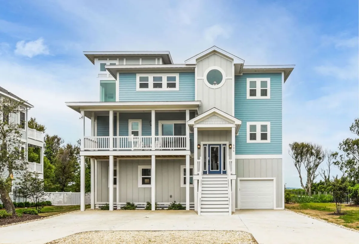A cheerful exterior shot of the home's spacious front porch, highlighting its inviting architectural design and light blue color scheme. The porch offers ample seating and space for guests to gather, relax, or enjoy the view.