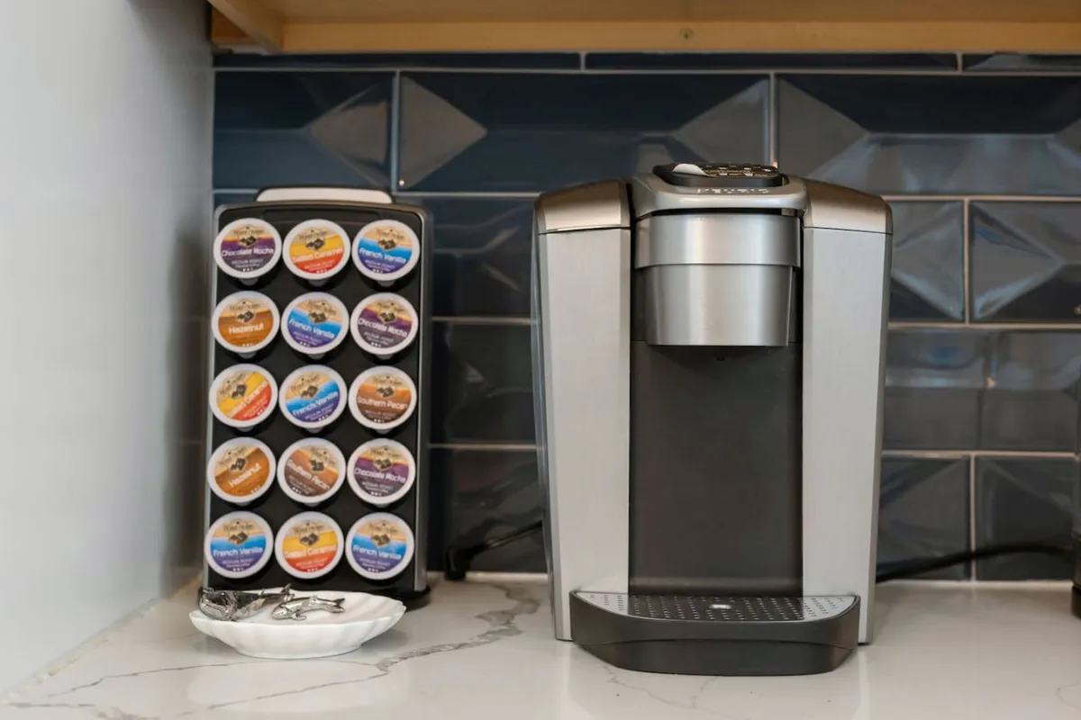A close-up of a Keurig coffee maker and a well-organized K-cup station on a marble countertop, creating a cozy coffee nook ideal for starting the day or socializing over a cup. The setup exudes warmth and convenience, inviting guests to enjoy a fresh brew anytime.