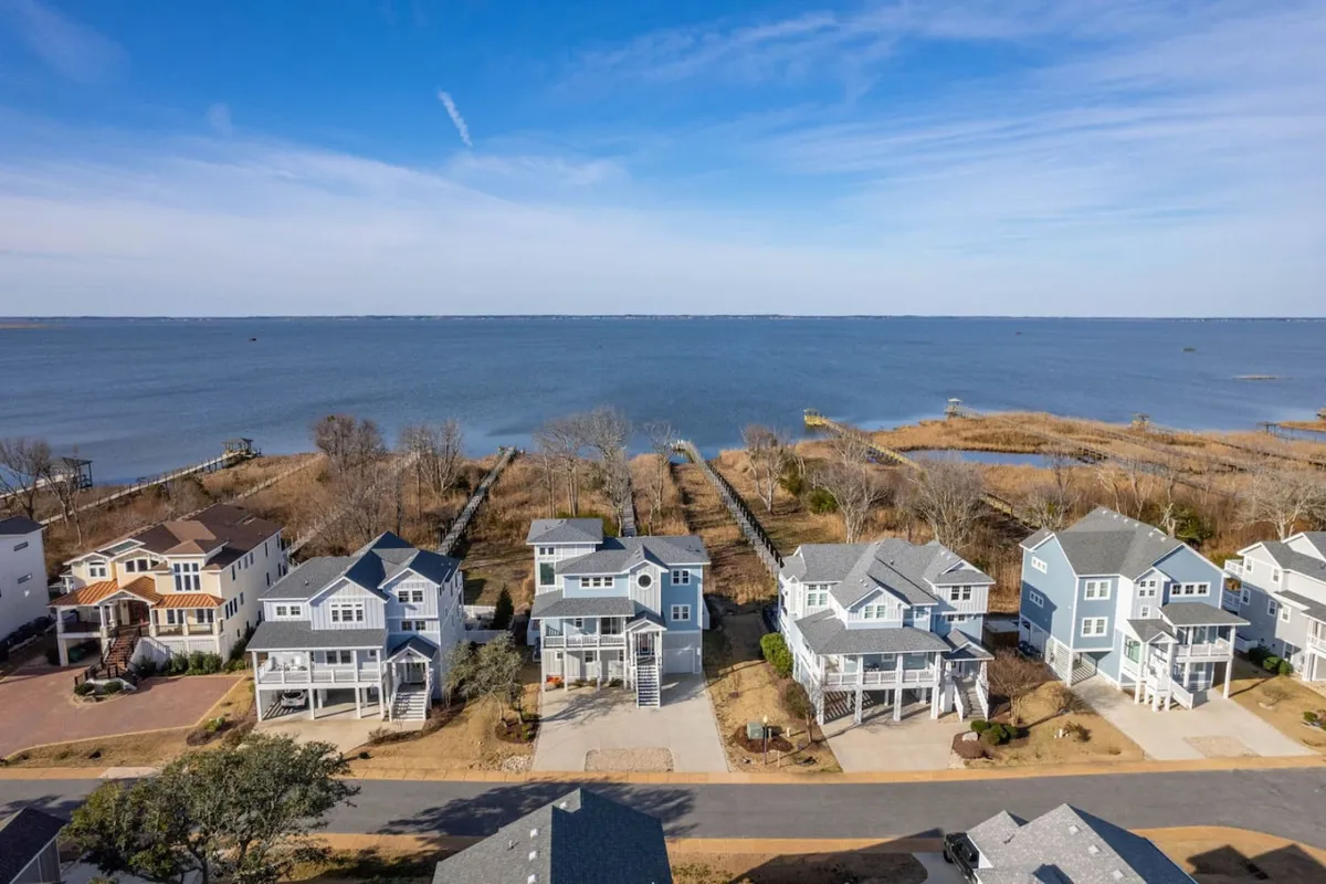 A panoramic view of the waterfront with a row of houses and a natural landscape backdrop. The scene suggests opportunities for boating, fishing, walking, and observing local wildlife, inviting guests to explore the area’s outdoor and community offerings.