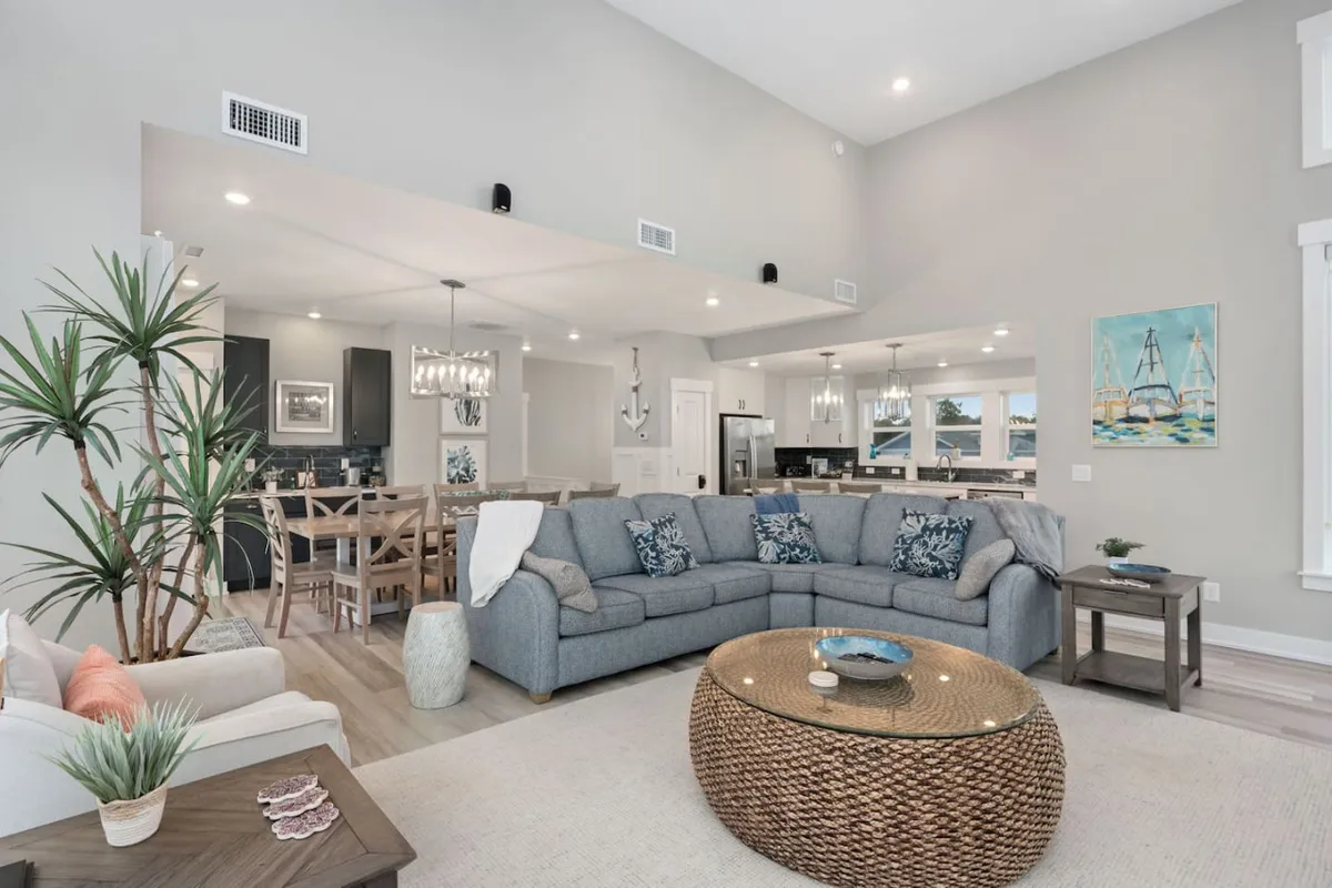 This image showcases a spacious living area with a sectional sofa, a coffee table, artwork on the wall, and a dining area visible in the background. The layout suggests an open-concept space ideal for gatherings, relaxing, and entertaining.