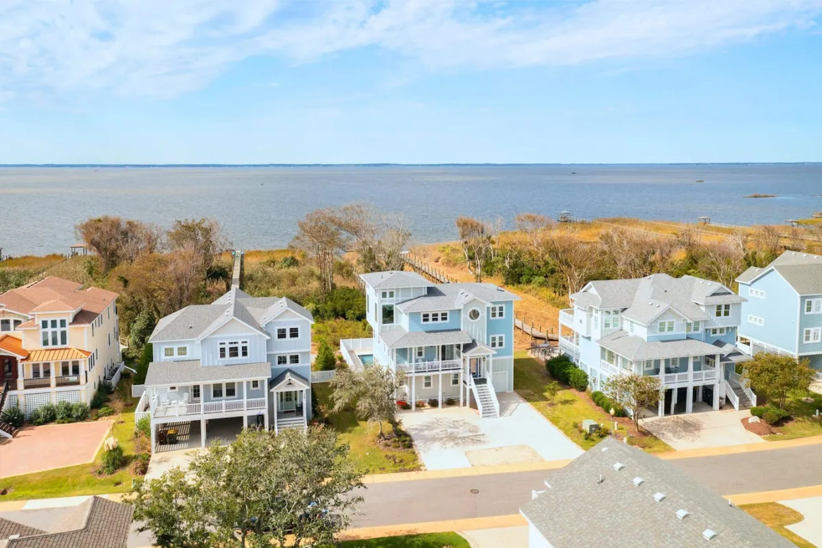 A peaceful exterior view of the waterfront, colorful houses, and green landscaping. The setting is perfect for leisurely fishing, boating, picnicking, and sunset watching, with a community feel and lush natural surroundings apparent.