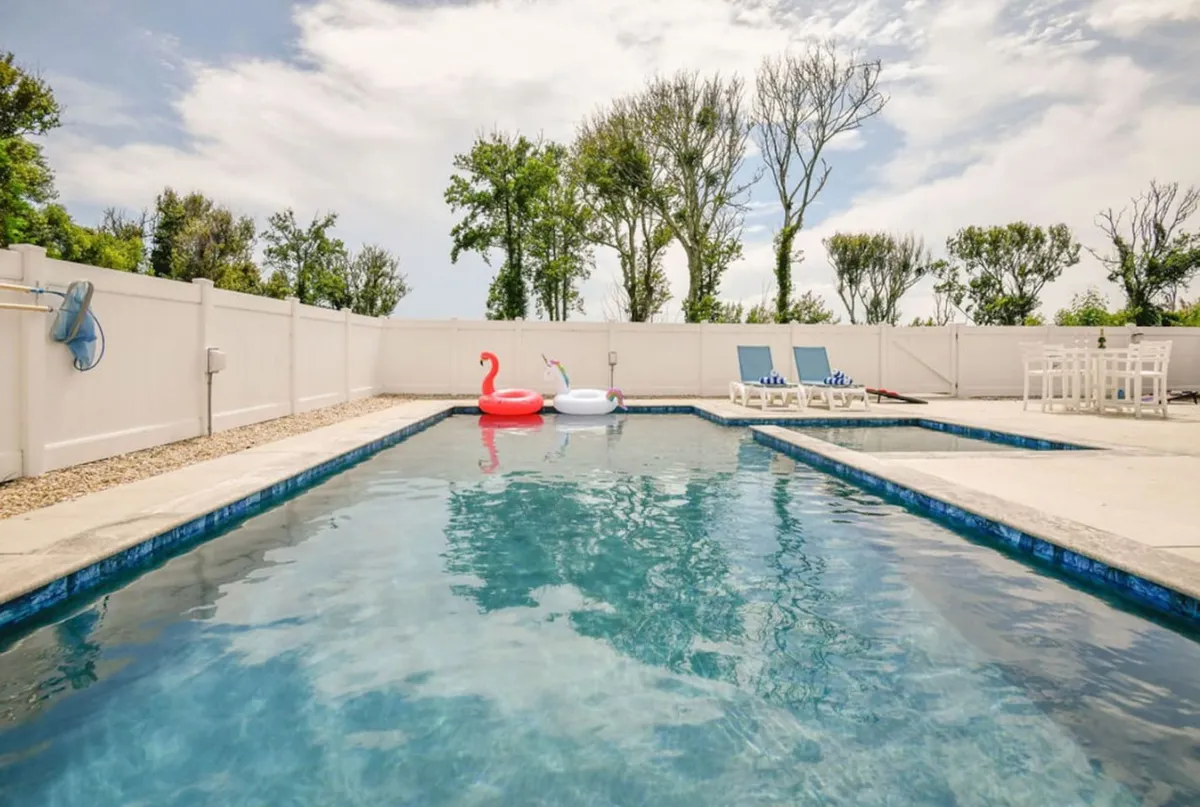 This lively exterior shot highlights the sparkling swimming pool adorned with playful inflatable floats, lounge chairs, and an outdoor dining area. The space is ready for sunbathing, swimming, or group gatherings, evoking classic vacation fun.
