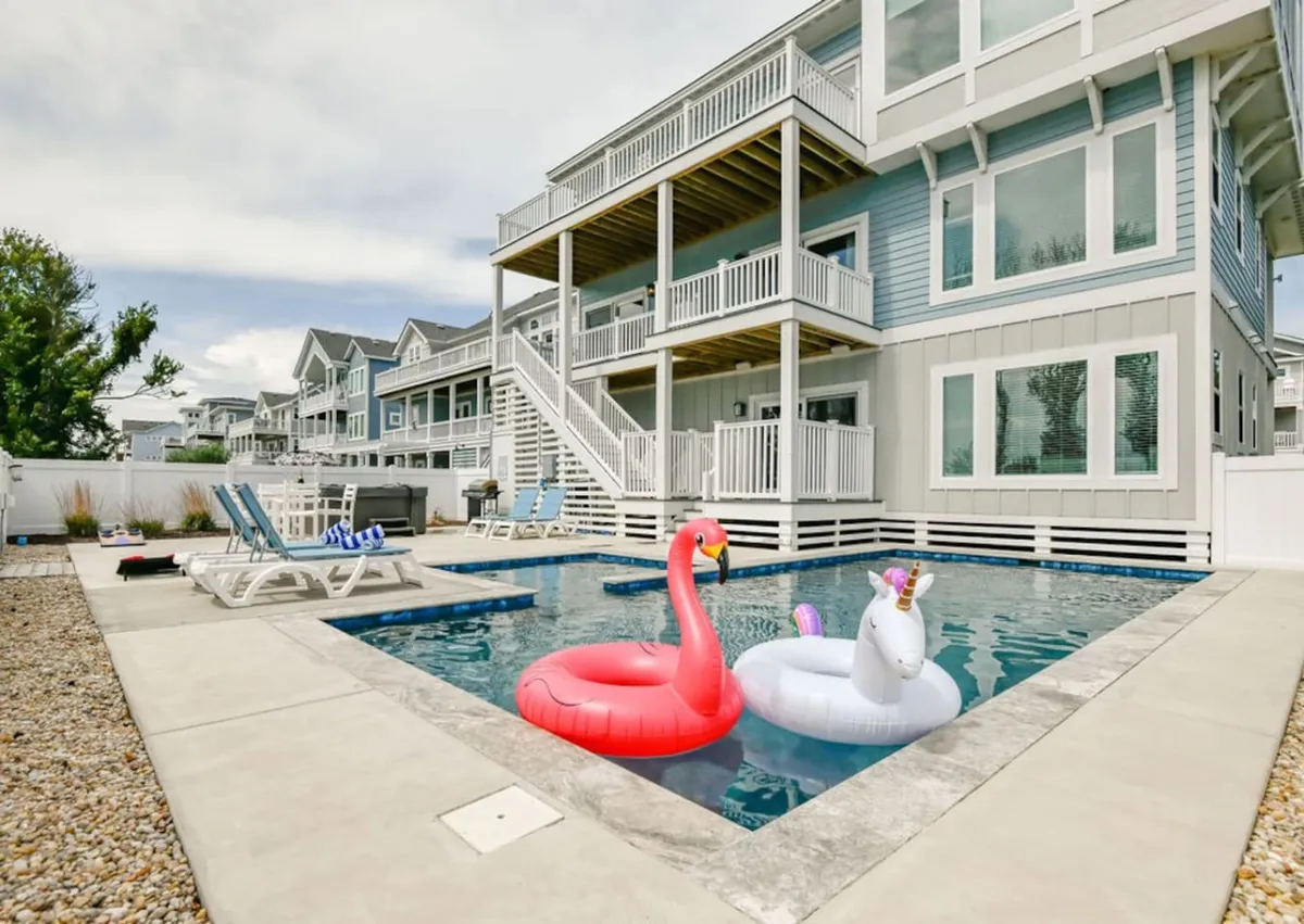 The pool area features an inflatable flamingo and unicorn, cozy deck chairs, and a balcony above. The setup suggests playful afternoons and lively gatherings with friends or family, all in a relaxing environment.